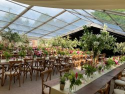 Beautifully decorated wedding marquee with floral arrangements, wooden tables, and chairs set for a luxury outdoor celebration.