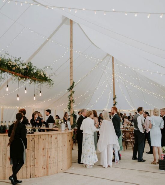 Traditional Pole Marquee with Rustic Wedding Bar Elegant traditional pole marquee with festoon lighting, a rustic wooden bar, and guests enjoying a sophisticated wedding celebration.